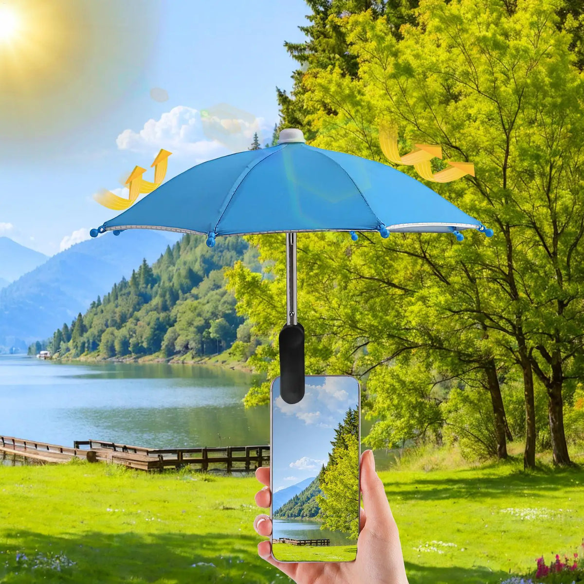 Eine Hand hält ein Smartphone unter einem blauen Clipsonnenschirm in einer sonnigen Landschaft mit Bergen und Bäumen.