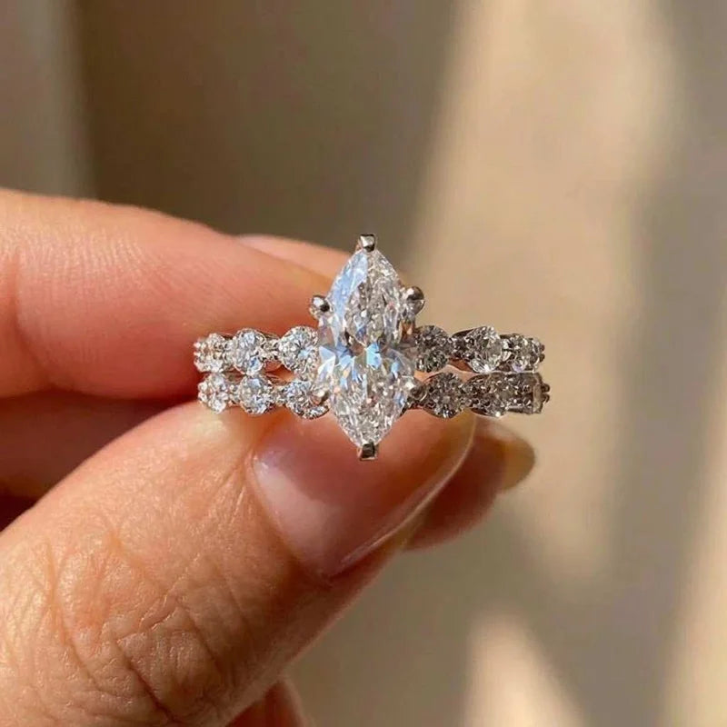 Une main tient une bague marquise en argent sterling avec une pierre centrale et des diamants pavés.