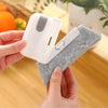 A hand holds a white 2-in-1 cleaning brush with a soft gray scouring head.