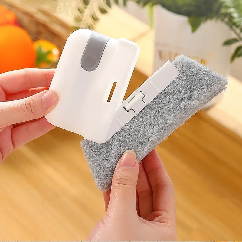 A hand holds a white 2-in-1 cleaning brush with a soft gray scouring head.