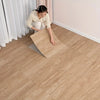 A woman is installing wood grain peel and stick vinyl flooring tiles on a light-colored floor.
