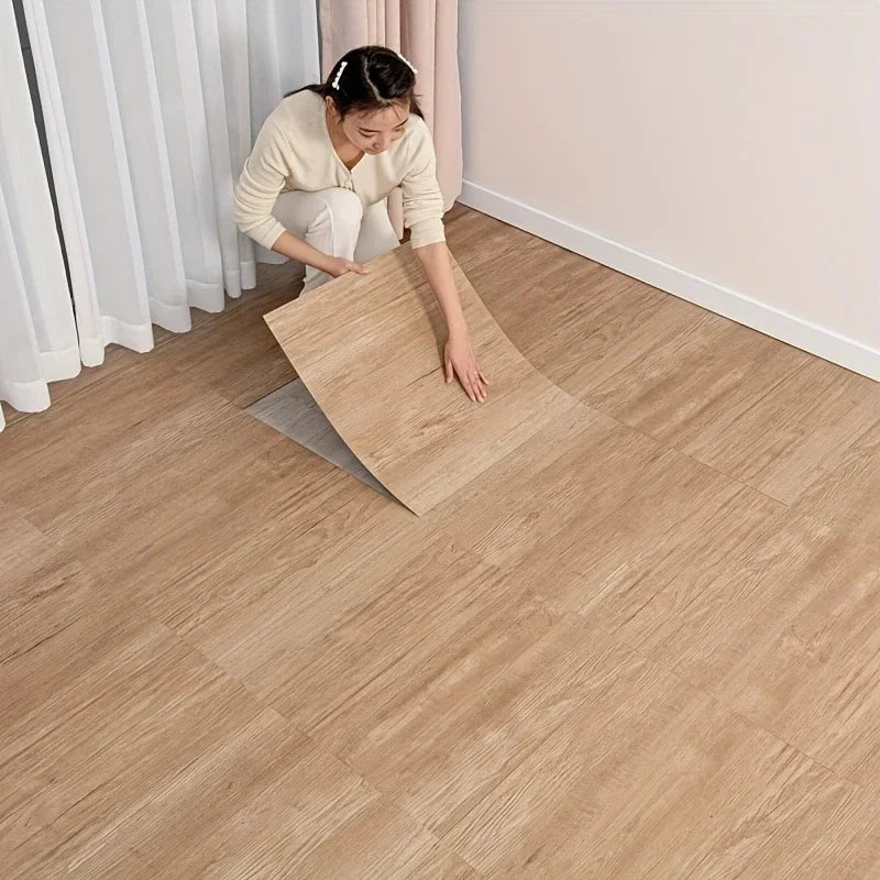 A woman is installing wood grain peel and stick vinyl flooring tiles on a light-colored floor.