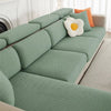 A light sage green jacquard elastic sofa slipcover with orange accent pillows on a white sofa.