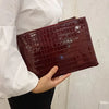 A person holds a dark burgundy crocodile-embossed PU leather envelope clutch.