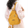 A woman is holding a mustard yellow waterproof nylon crossbody sling bag against a light pink shirt.