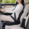 A woman is sitting in a car seat with a white top, driving, and using an ergonomic memory foam seat cushion.