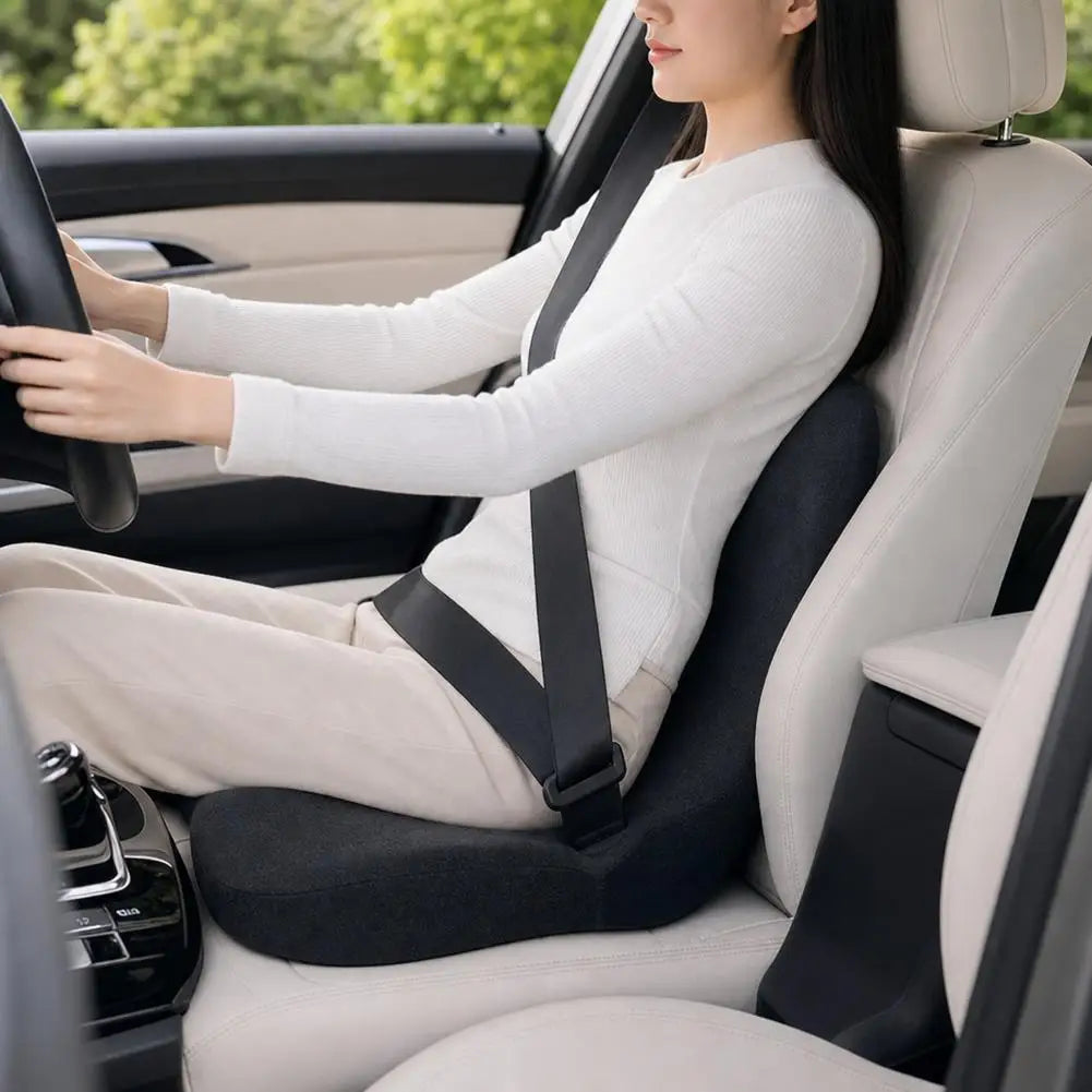 A woman is sitting in a car seat with a white top, driving, and using an ergonomic memory foam seat cushion.