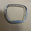 A chrome steering wheel cover with an emblem placed on a light brown surface.