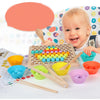 A baby is smiling while interacting with a wooden bead maze puzzle and various colored beads and tools.
