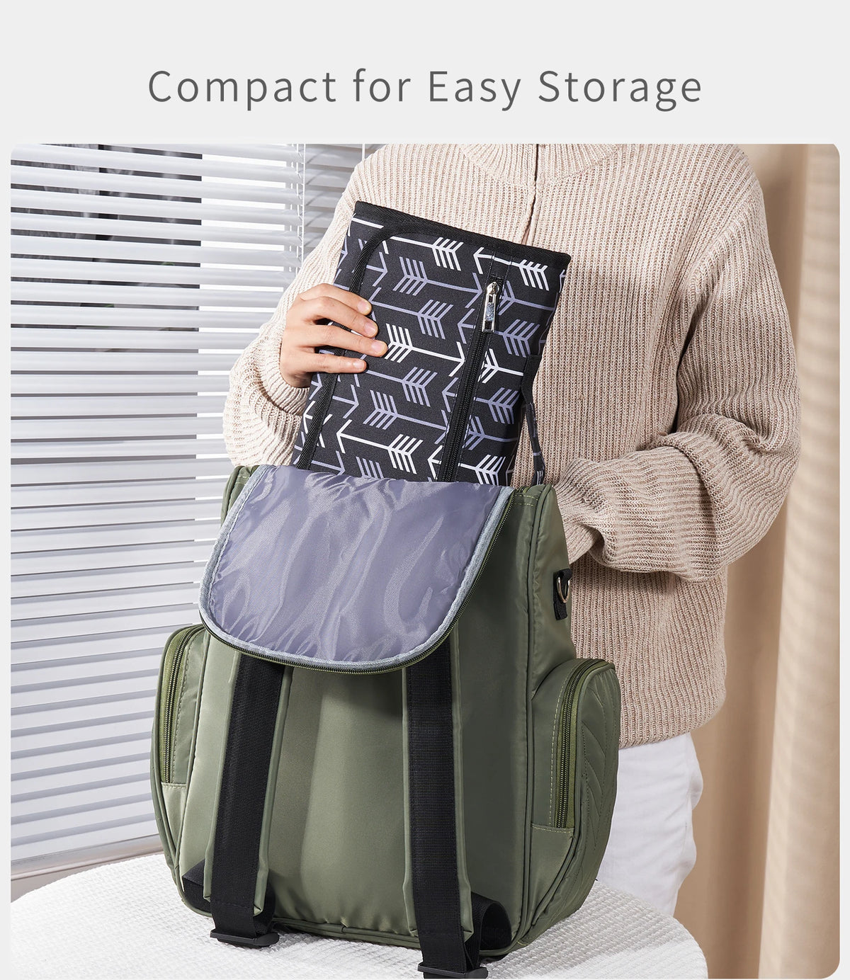 A person is holding a compact, olive green foldable waterproof baby changing pad bag.