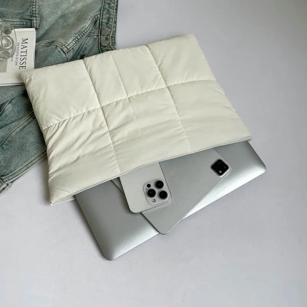 Un bolso de mano acolchado blanco con cierre de cremallera sobre una computadora portátil plateada.