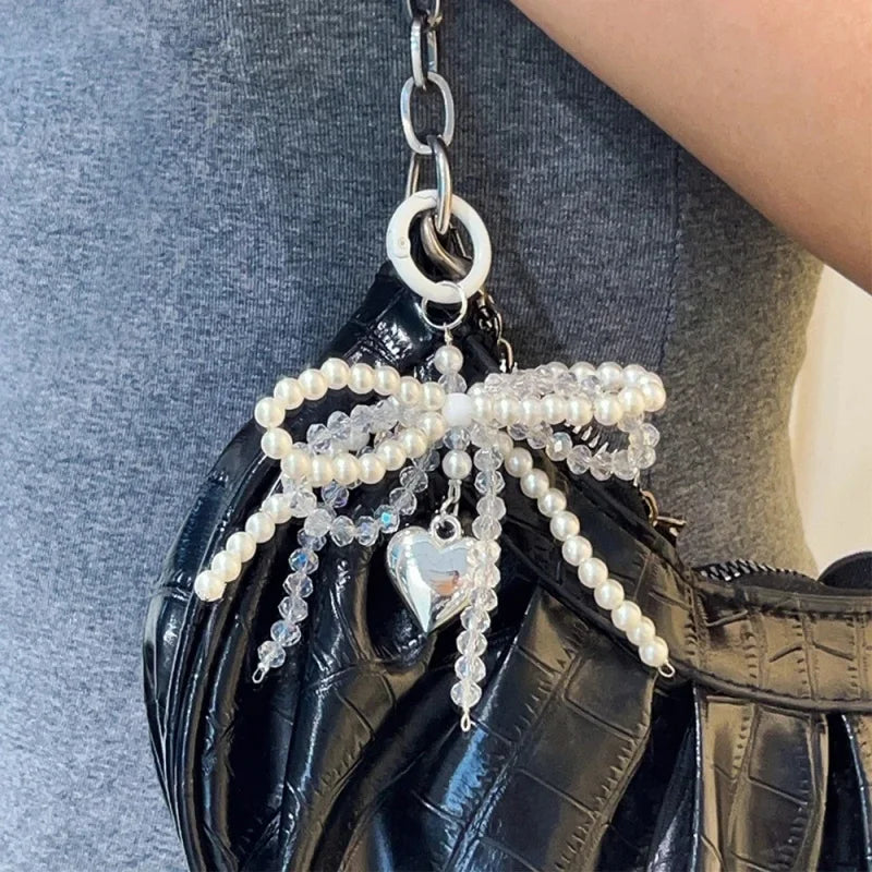 A black faux leather bag decorated with a pearl bow keychain featuring a heart charm.