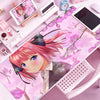 A pink anime character illustration on a mouse pad featuring pink hair and a school uniform, placed on a desk with electronic