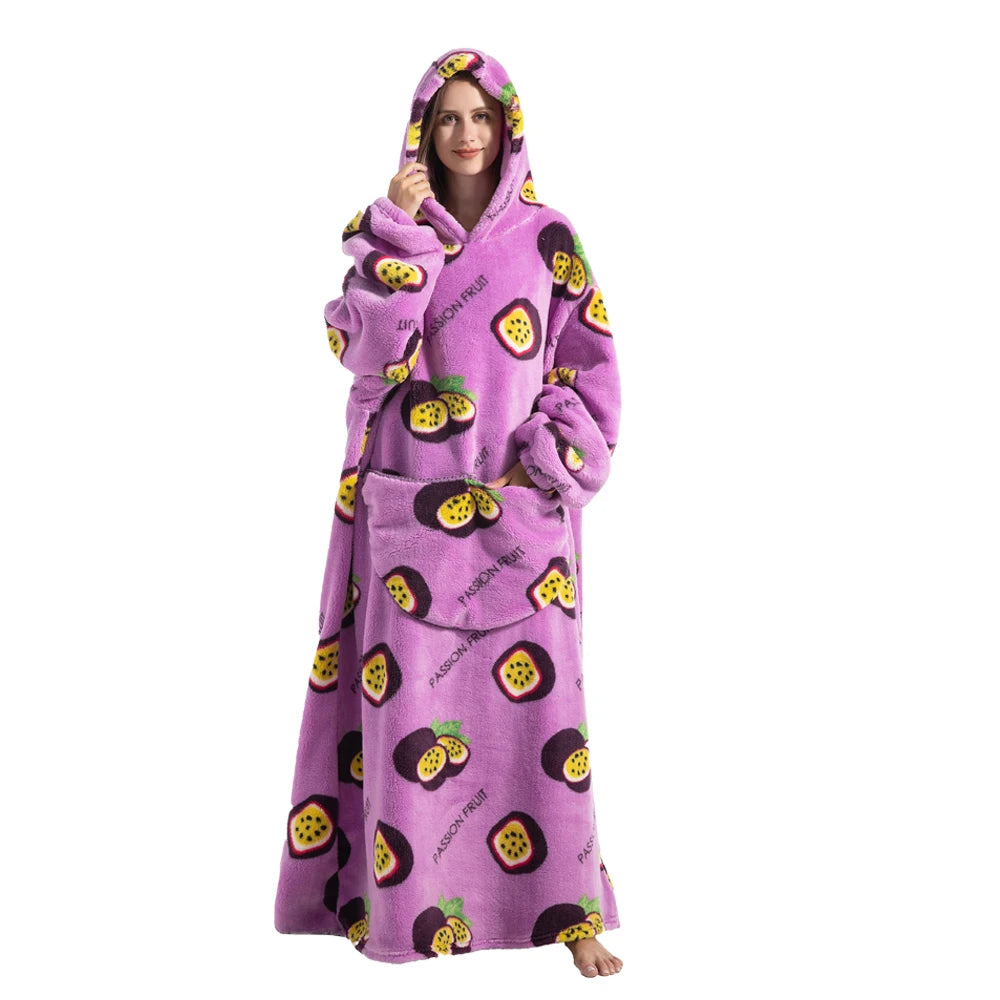 A woman wearing a purple oversized wearable blanket hoodie with a hood and sleeves, featuring a pattern of sliced fruit.
