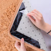 A hand is gripping a reusable non-slip rug gripper, which is black and white patterned, against a fluffy orange rug.