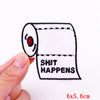 A white fabric roll with black embroidery that reads SHIT HAPPENS
