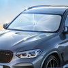 A close-up of a silver car's front windshield with a clear foldable sunshade installed for interior protection.