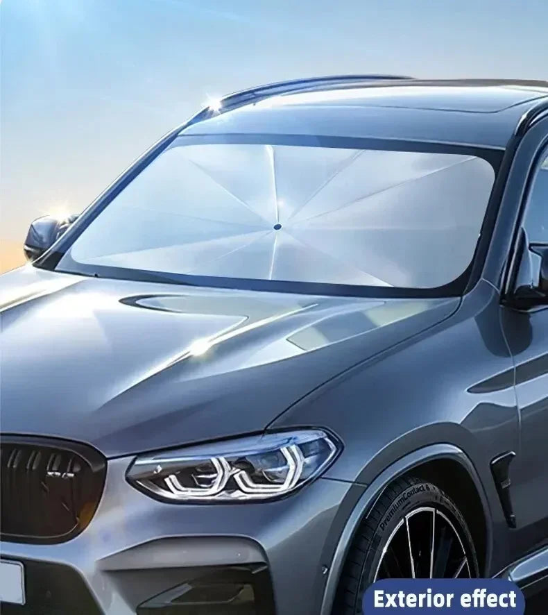A close-up of a silver car's front windshield with a clear foldable sunshade installed for interior protection.