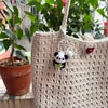 A handmade crochet bag with a white panda charm keychain hanging from the strap.