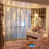 A window decorated with sheer curtains illuminated by warm fairy lights and a silver mirror.