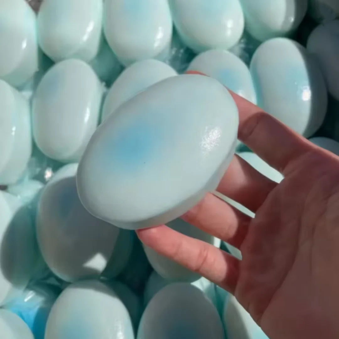 A hand holds a light blue silicone squishy fidget toy surrounded by many similar toys.