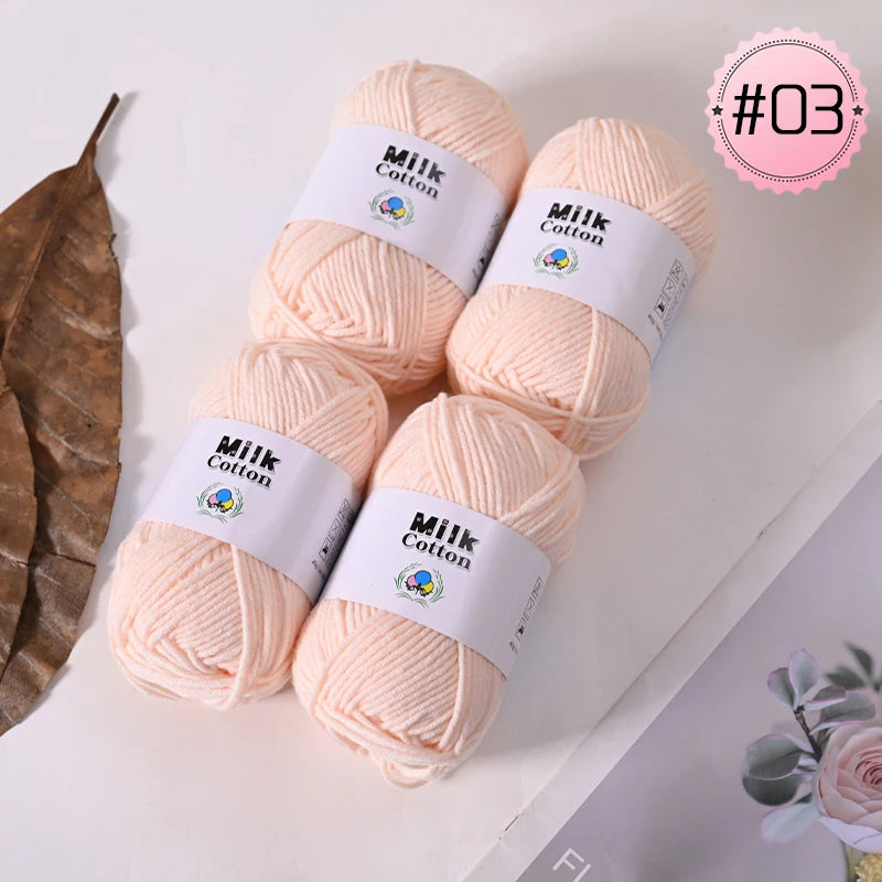 A pile of pink Milk Cotton yarn balls is displayed on a white surface with a brown leaf and a pink circular label.