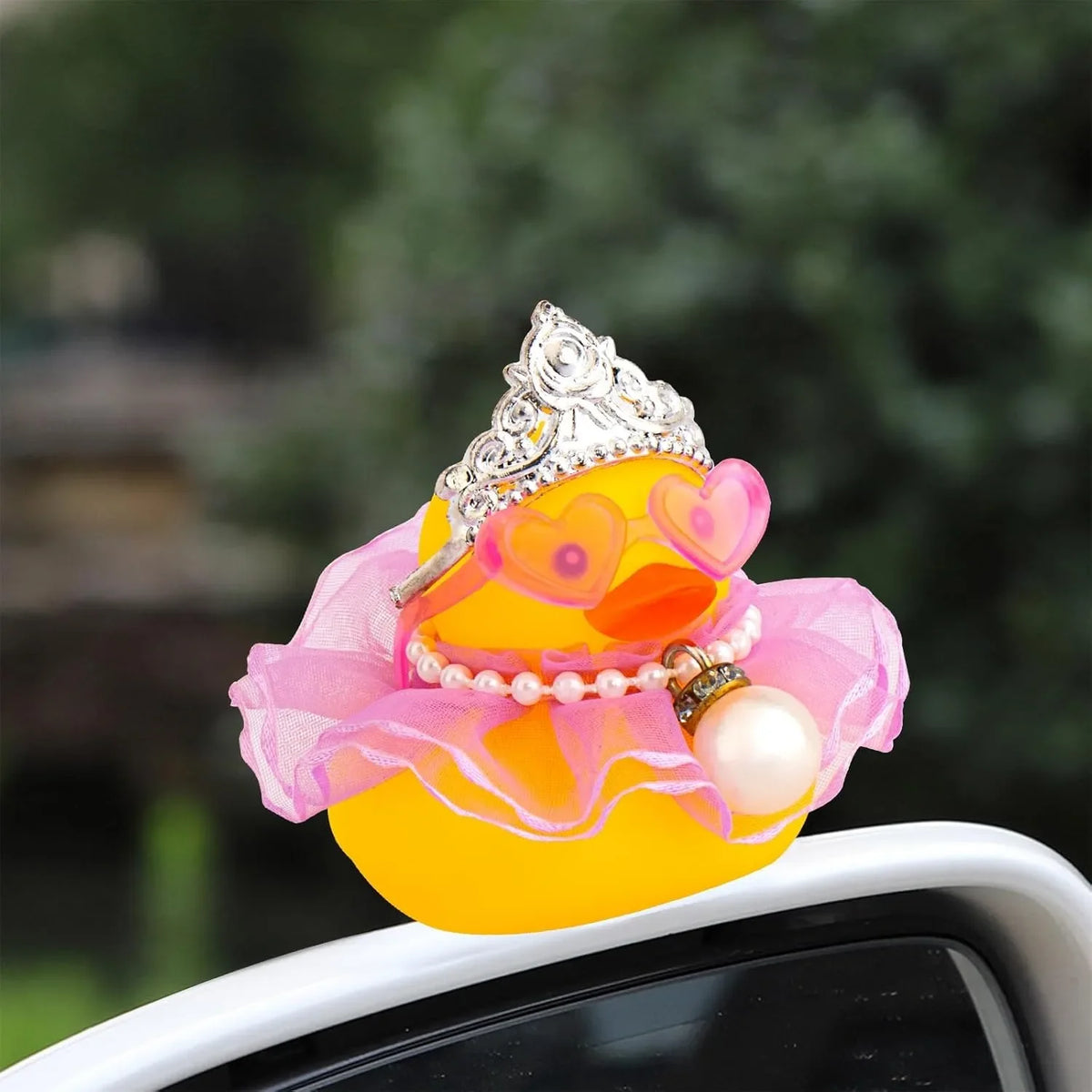 A rubber duck decoration featuring a crown, sunglasses, and a pearl necklace on a car surface.