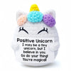 A handmade crochet unicorn doll with a yellow horn and pastel colored ears, holding a card that says I may be a tiny unicorn 