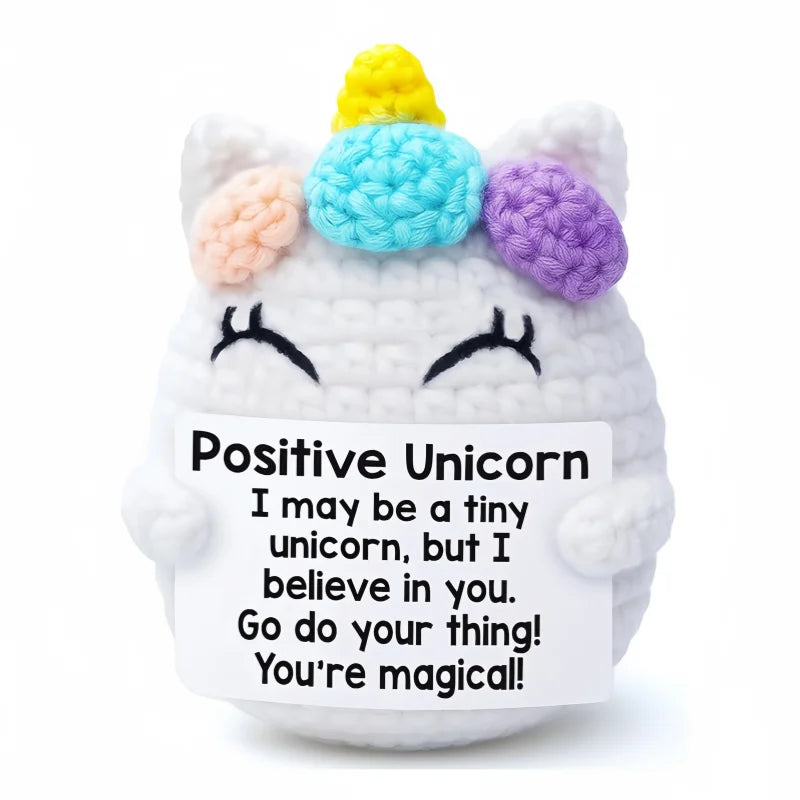 A handmade crochet unicorn doll with a yellow horn and pastel colored ears, holding a card that says I may be a tiny unicorn 
