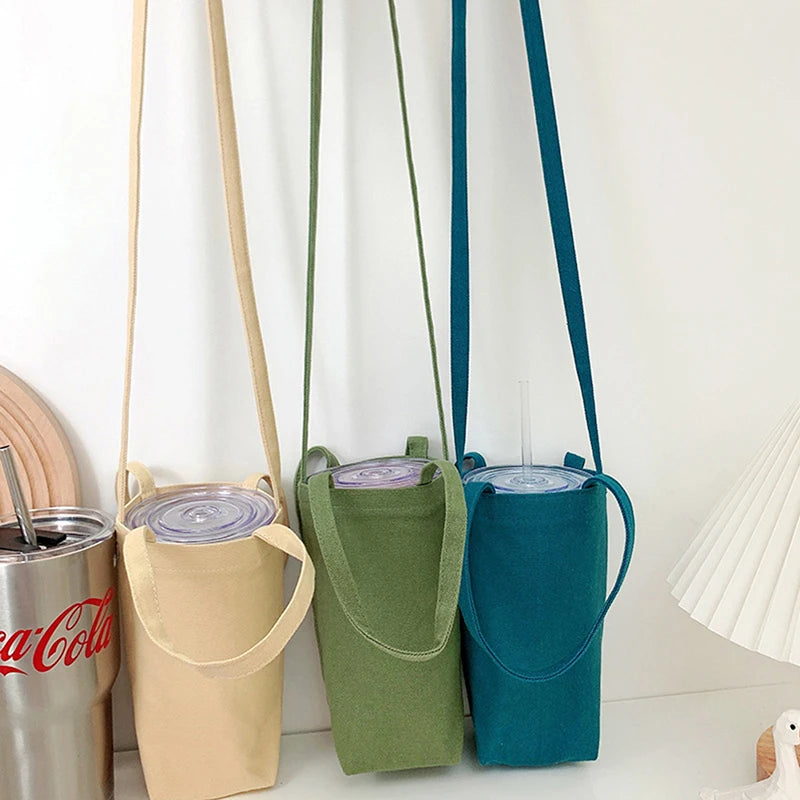 Three canvas water bottles in beige, olive green, and teal hanging on a white wall.