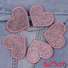 A set of five pink glitter heart and star iron-on embroidered patches on a denim fabric background.