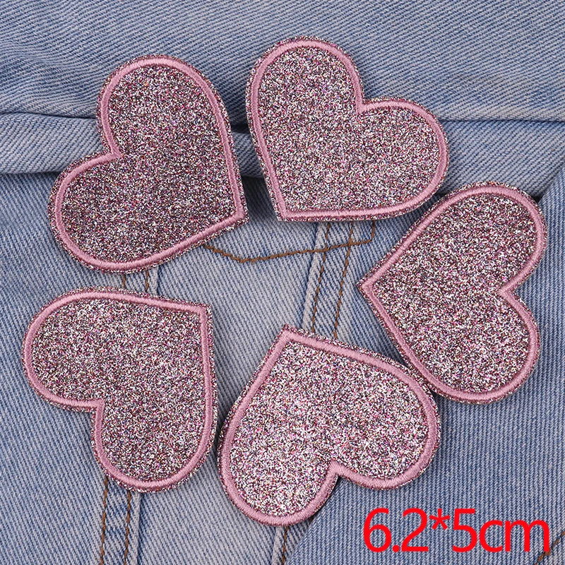 A set of five pink glitter heart and star iron-on embroidered patches on a denim fabric background.