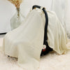 A beige breathable cotton muslin car seat and stroller cover draped over a white fluffy surface.