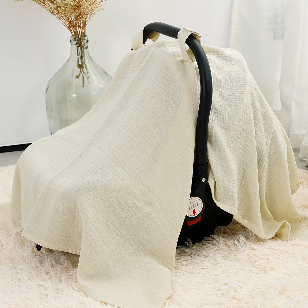 A beige breathable cotton muslin car seat and stroller cover draped over a white fluffy surface.