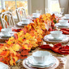 An artificial maple leaf garland in vibrant autumn colors, including orange, yellow, and red leaves, displayed on a wooden ta