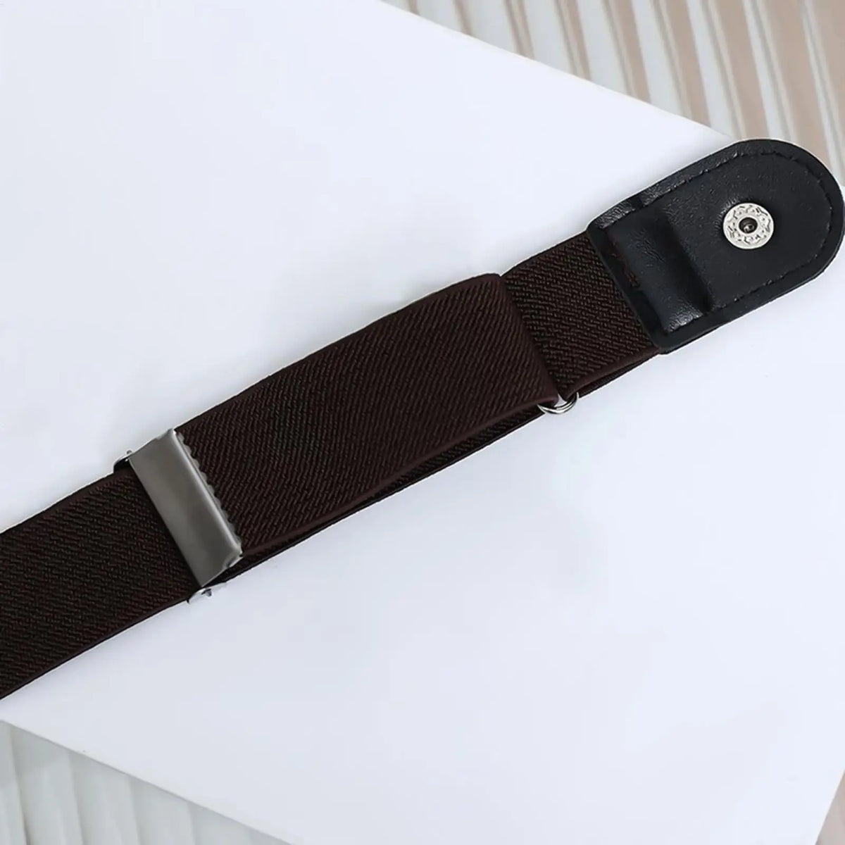 A close-up view of a black elastic belt strap with a silver buckle, laid on a white surface.