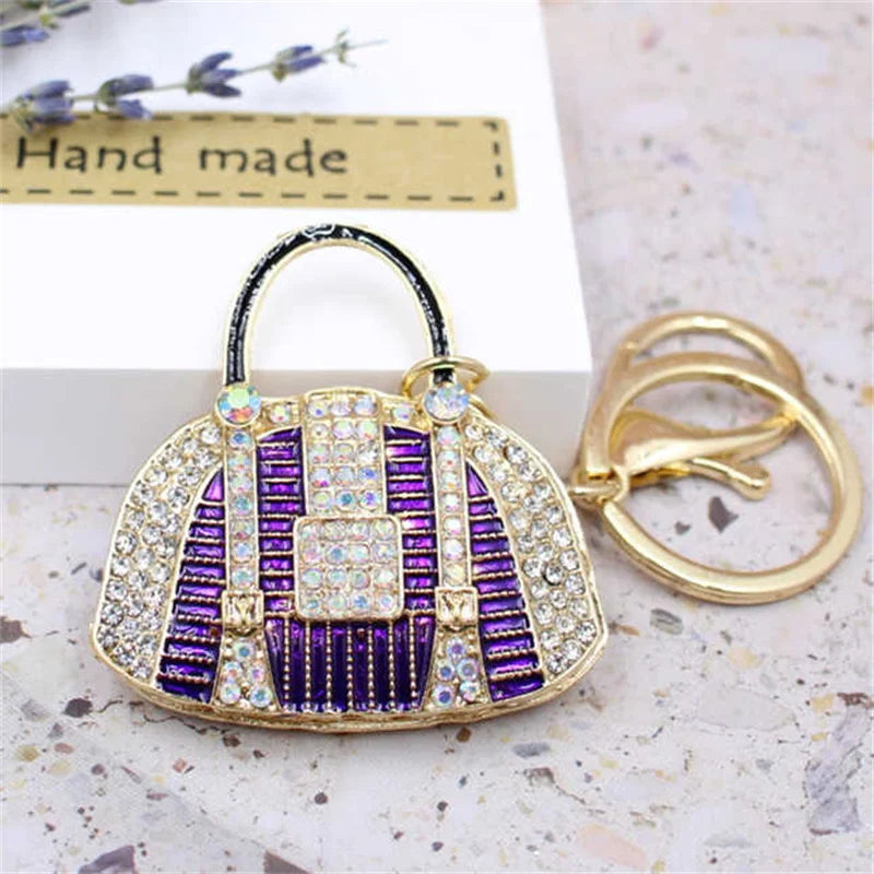 A crystal rhinestone handbag keychain featuring purple and white stripes on a gold-toned metal ring.