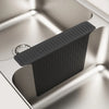 A black silicone sink protector mat with drainage holes is placed in a stainless steel kitchen sink.