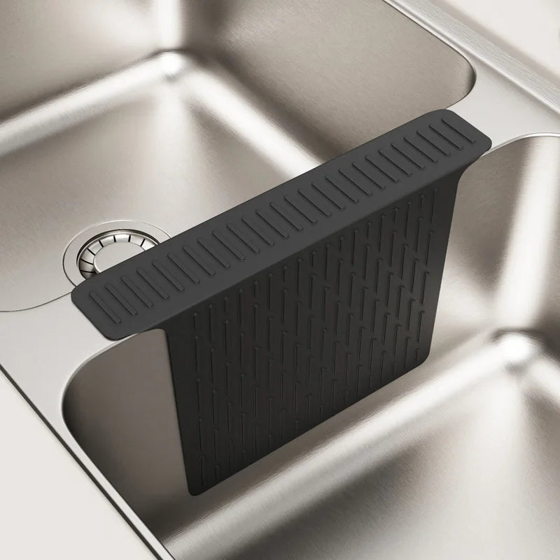A black silicone sink protector mat with drainage holes is placed in a stainless steel kitchen sink.