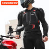 A person wearing a black motocross armor jacket with chest and back protection standing next to a red motorcycle.