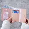 A hand holds a pink slim triple-fold PU leather wallet with a VISA card and cash inside.