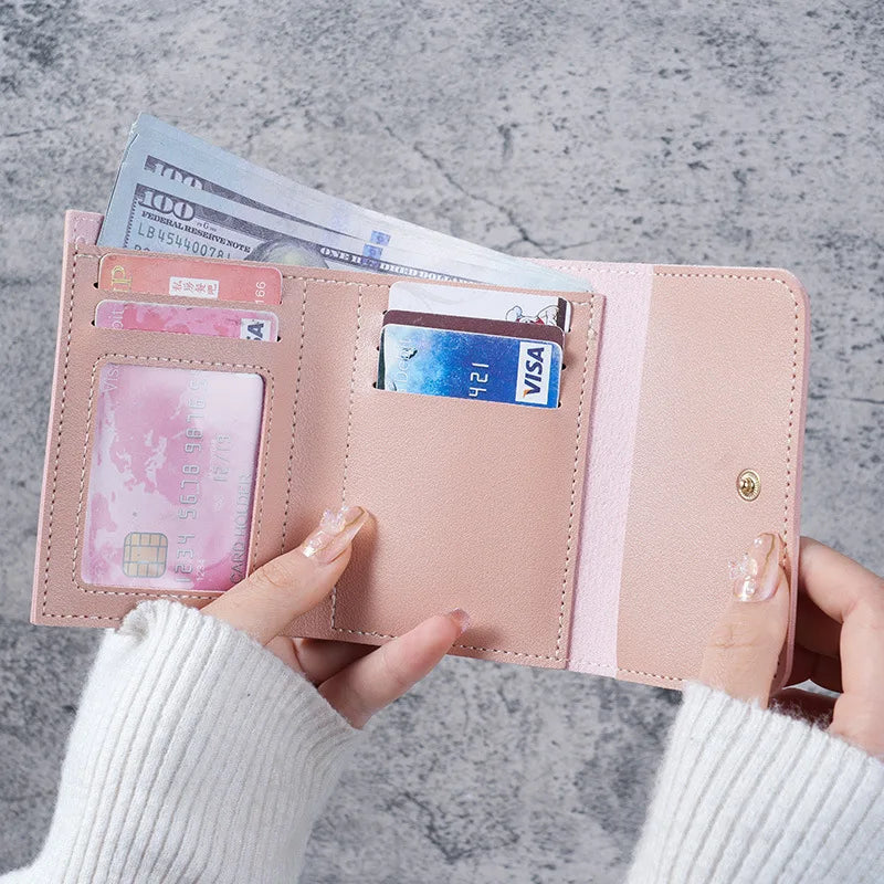 A hand holds a pink slim triple-fold PU leather wallet with a VISA card and cash inside.