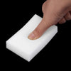 A hand is pressing down on a white melamine sponge cleaning eraser.