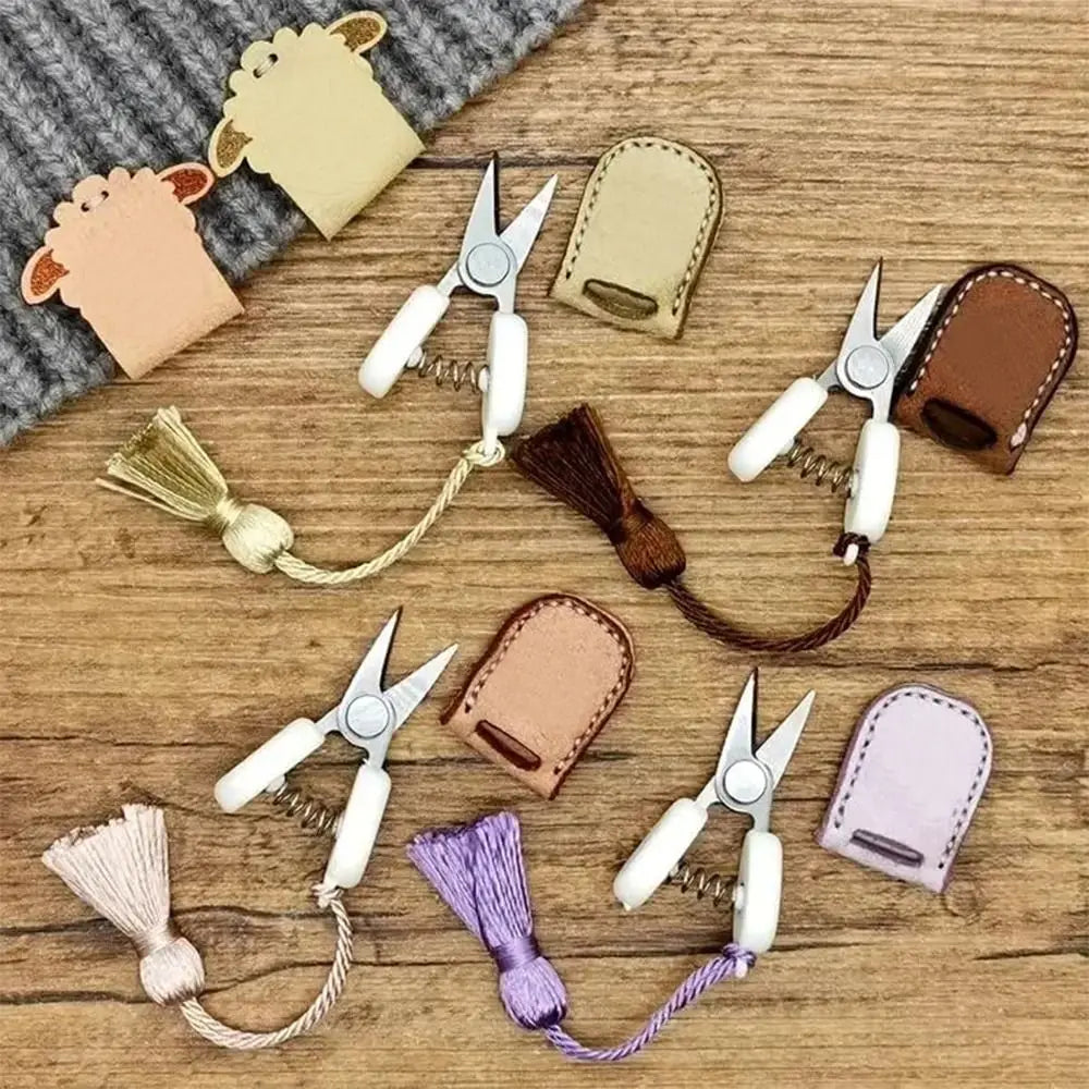 A collection of precision mini scissors with protective leather covers and decorative tassels arranged on a wooden surface.