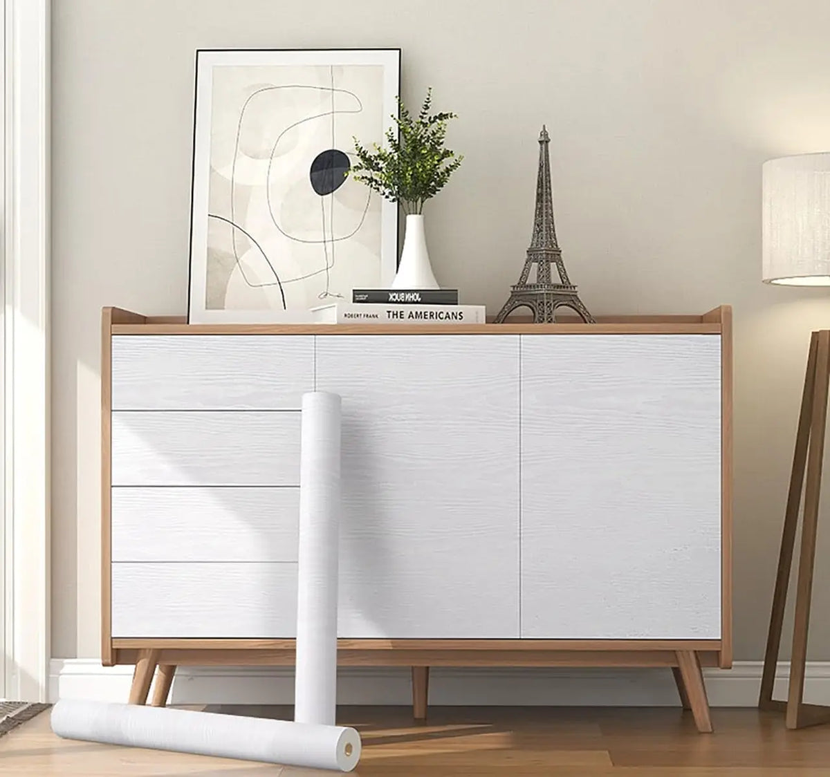 A roll of self-adhesive wood grain wallpaper displayed on a wooden cabinet with decorative items.