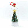 A clear glass message bottle shaped like a Christmas tree with a snowy scene and a red cap.