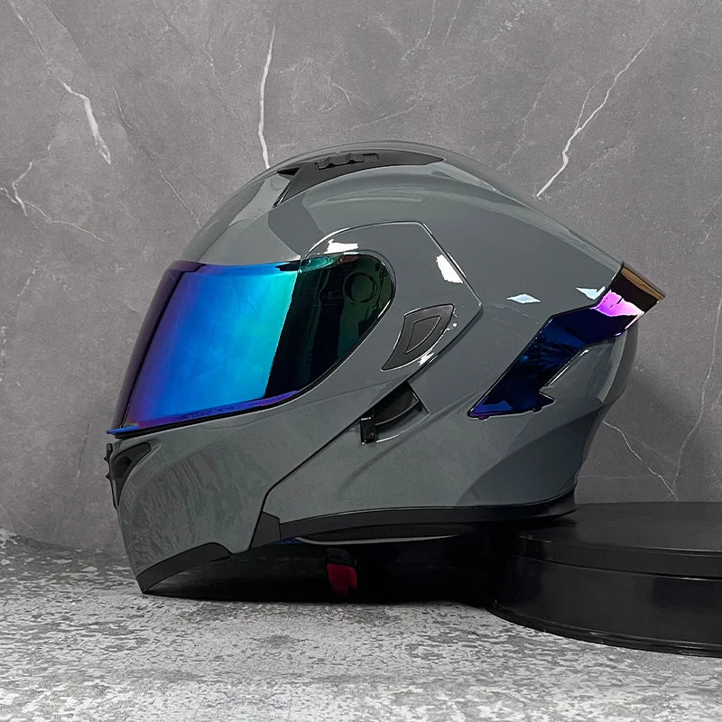 A dark gray modular flip-up motorcycle helmet with a reflective blue visor displayed against a gray stone background.
