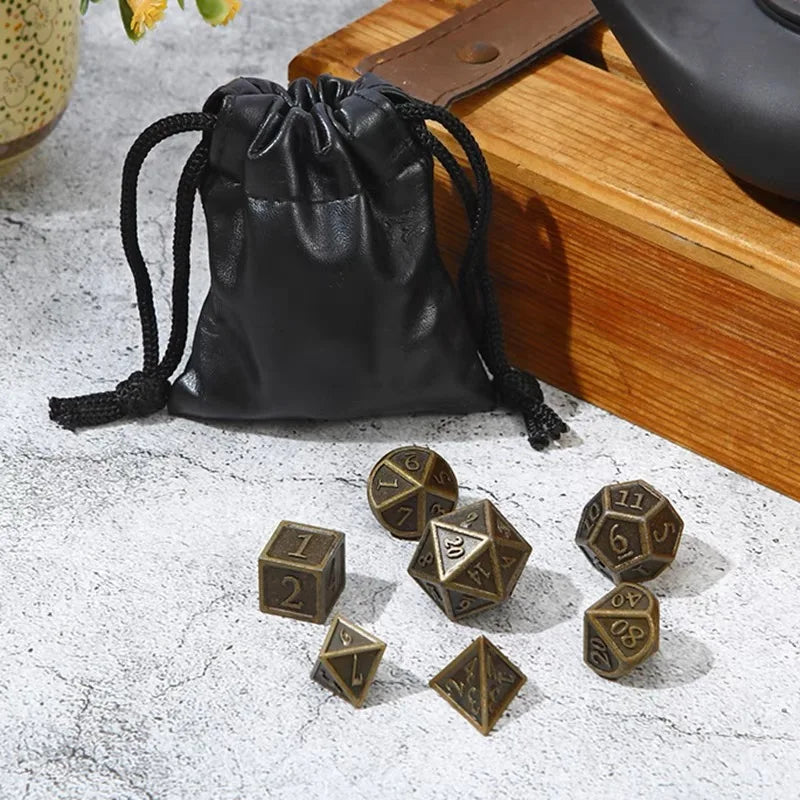 A black leather drawstring pouch next to a set of bronze metal polyhedral dice.