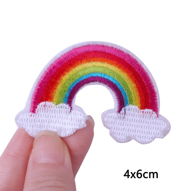 A hand holds a colorful rainbow cloud embroidery patch for iron-on use.