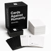 A black box of Cards Against Humanity with several stacks of white cards displayed on a white surface.